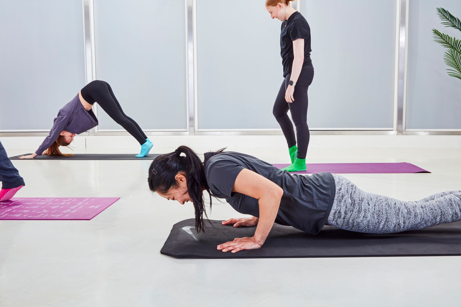 A diverse group of people performing different exercises like push-ups and yoga on various mats in a studio.