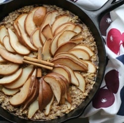 Healthy spiced pear baked oatmeal topped with whole walnut halves, prepared in a rustic cast iron skillet.