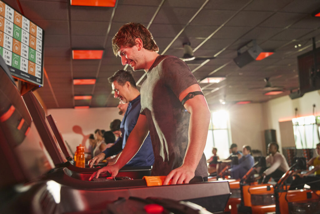 A person running on an Orangetheory-branded treadmill with focus and intensity.