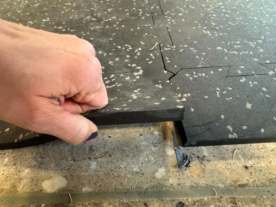 Close-up of a person lifting the corner of a thick black rubber mat to check its density.