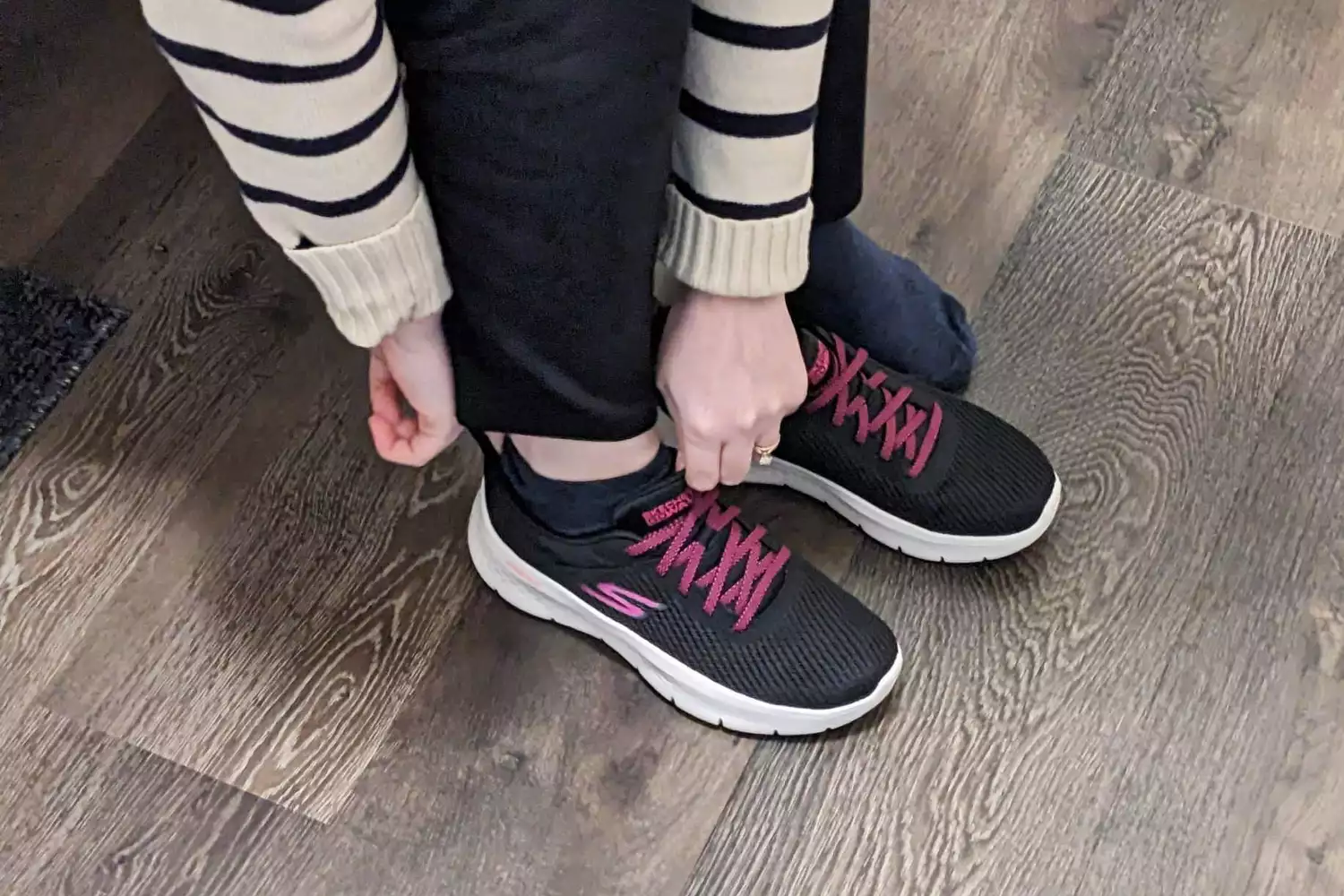 A person adjusting the laces on a pair of black and pink Skechers walking shoes.