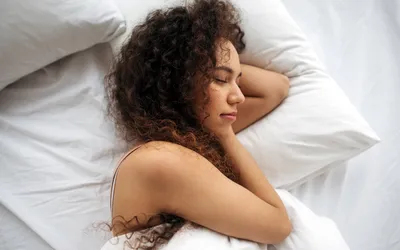 A woman sleeping peacefully in a white bed, symbolizing wellness and recovery.