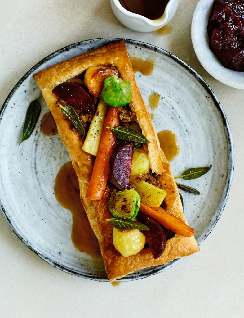 A golden-brown vegan roast dinner tart topped with seasonal roasted vegetables.