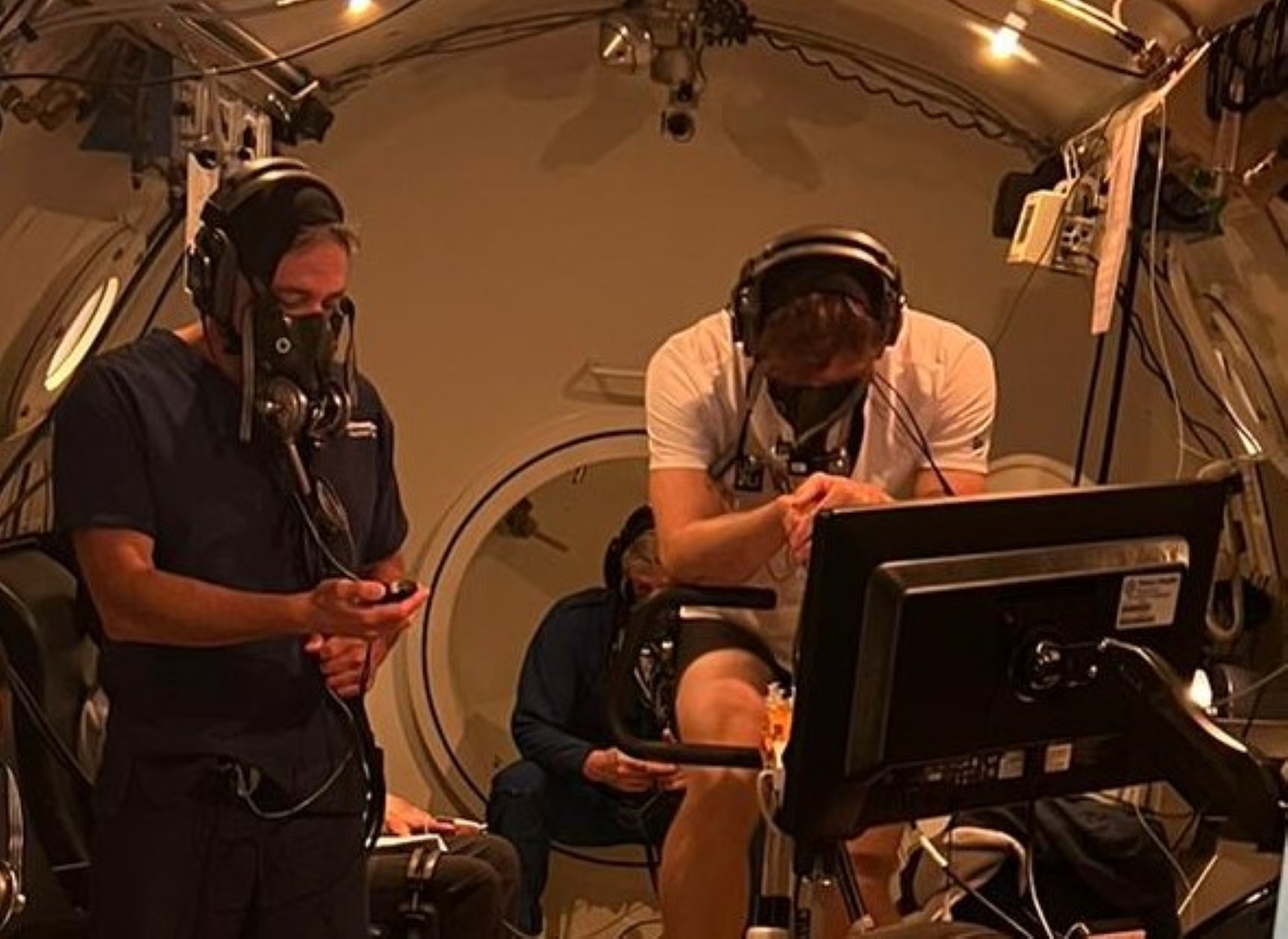 An athlete using a stationary bike inside a large hyperbaric chamber for research.