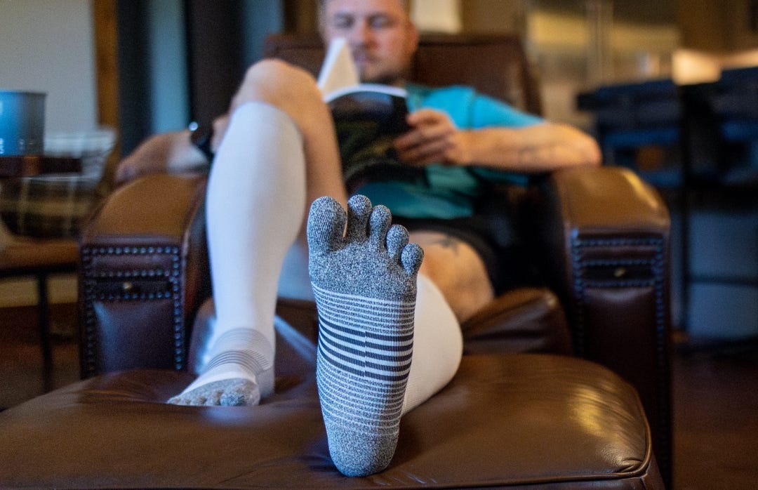 A man resting on a sofa wearing black athletic compression socks.