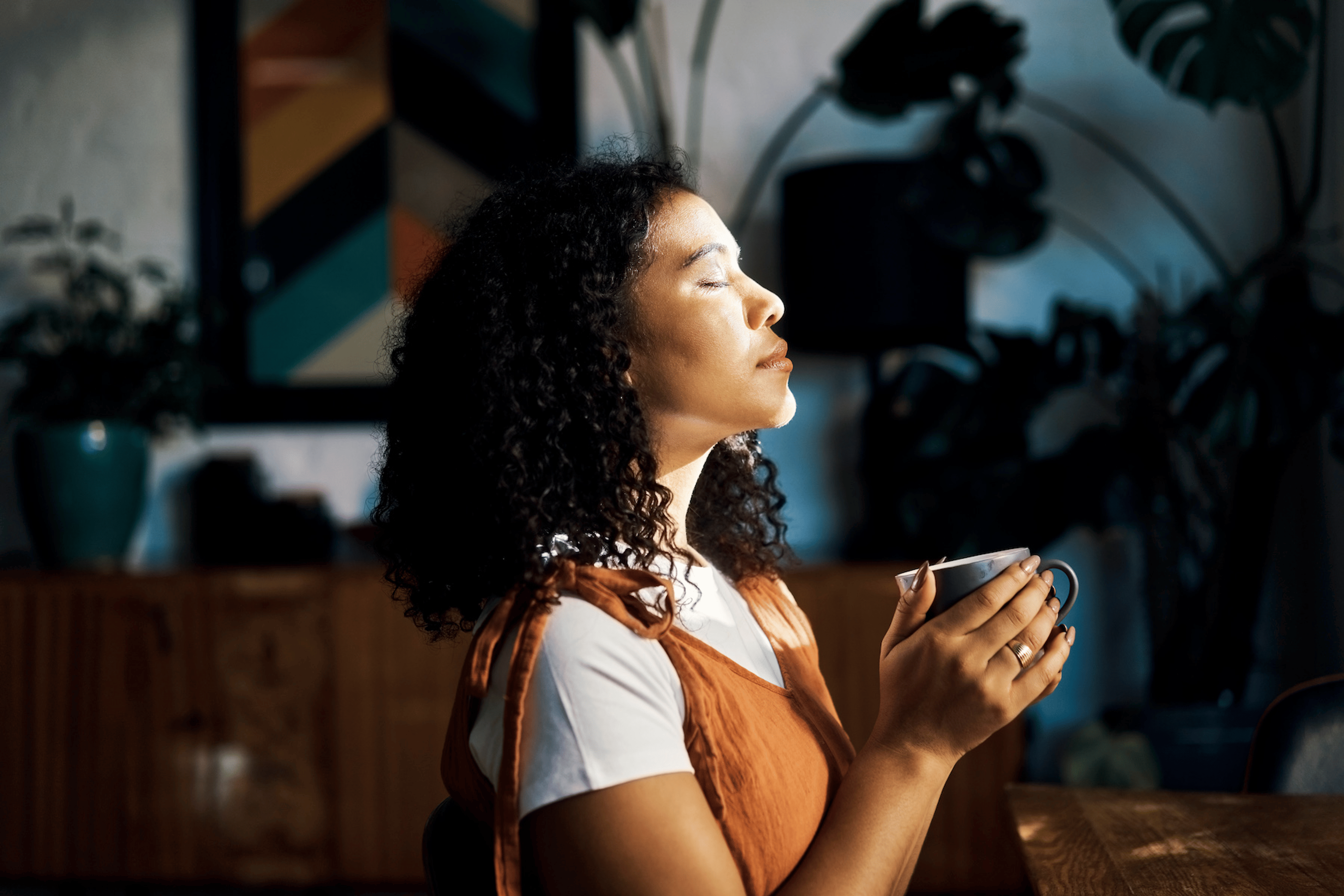 A woman sitting peacefully with a cup of coffee and closed eyes, practicing mindfulness.