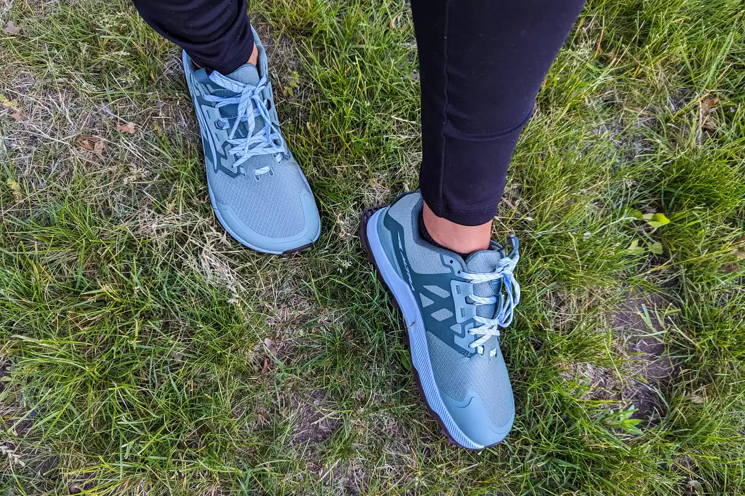 A person wearing Altra Lone Peak trail shoes standing on green grass.