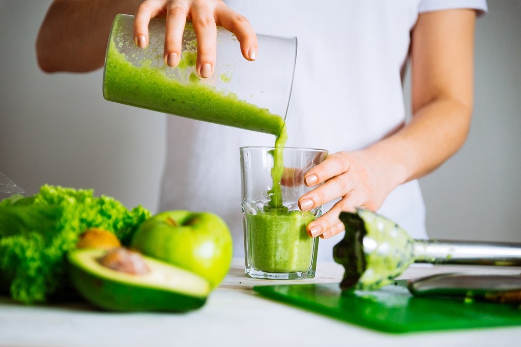 A person pouring a freshly blended green smoothie into a glass.