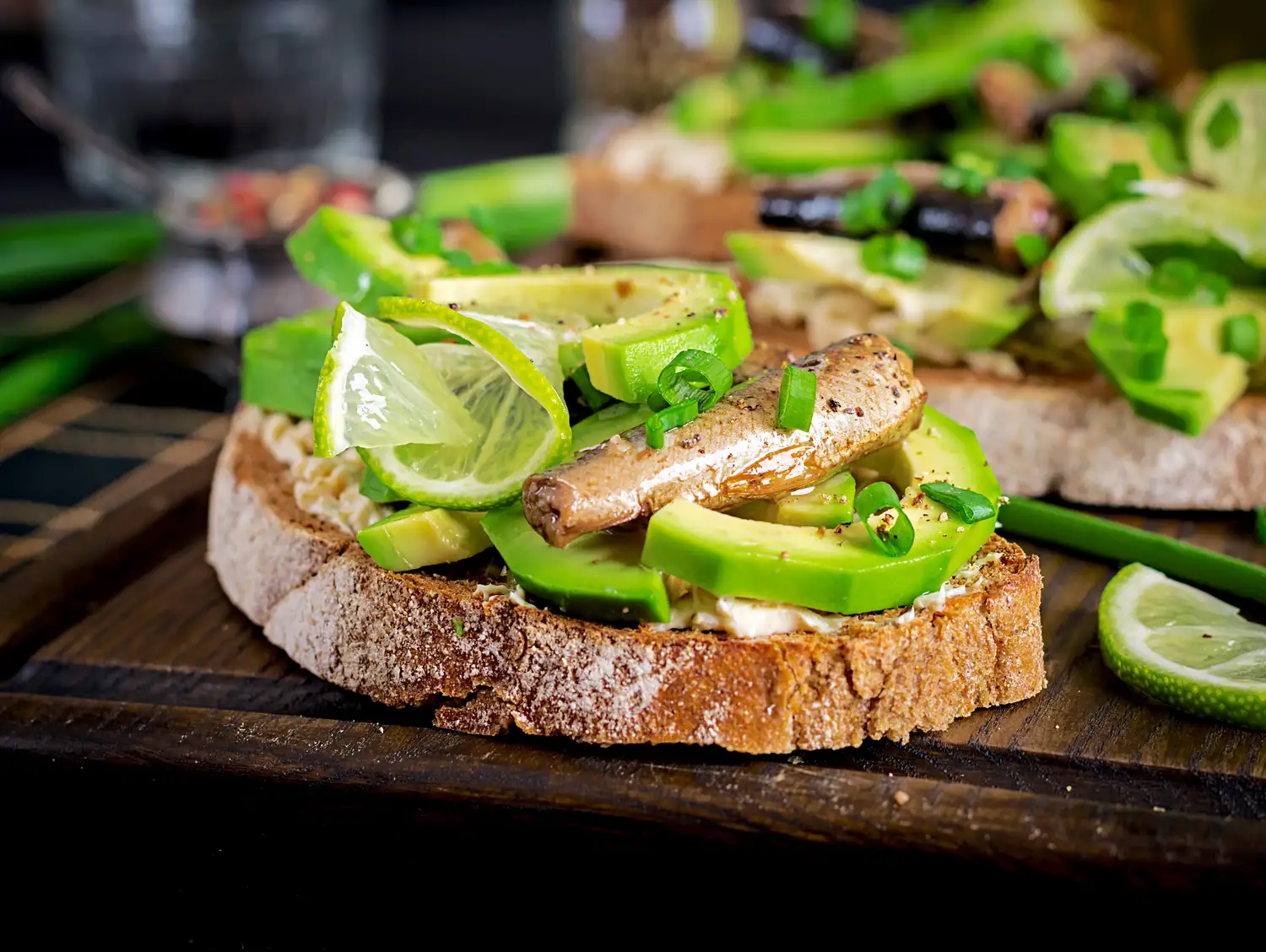 Sardine and avocado open-faced sandwiches on a wooden board.