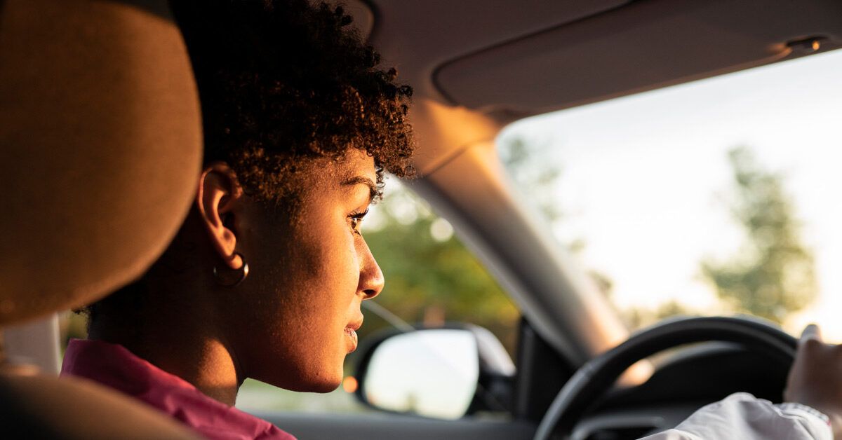 A woman driving a car attentively during golden hour, focused on the road.