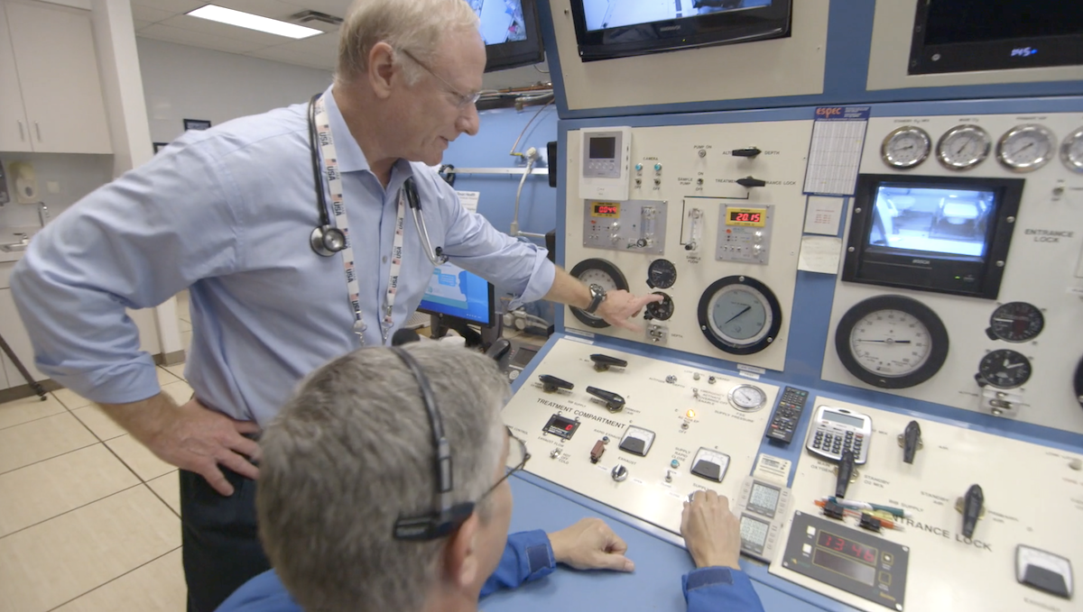 A physician inside a hyperbaric chamber interacting with a patient.