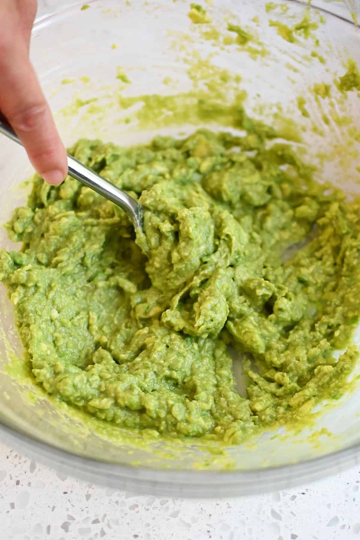Smoothly mashed seasoned avocado in a bowl ready for salad dressing.