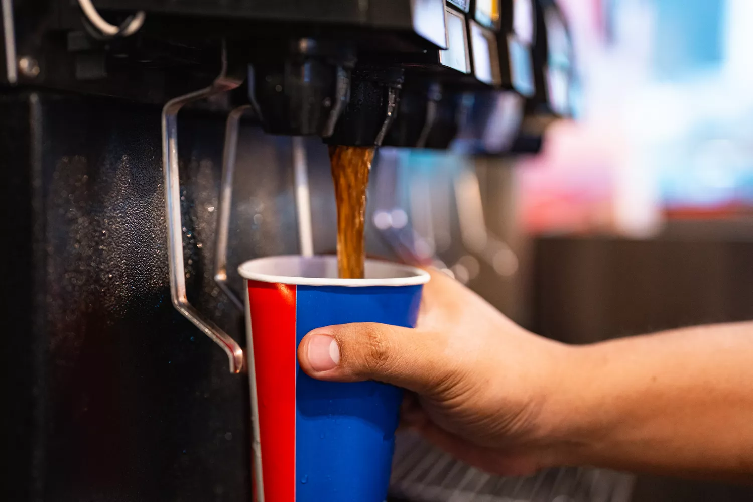 A person filling a large cup with sugary soda from a fountain machine.