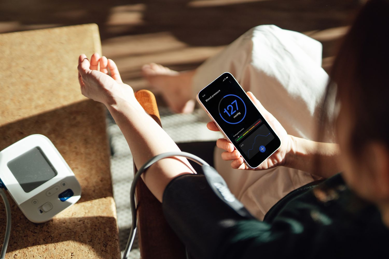 A person using a smartphone to track their blood pressure with a digital monitor.