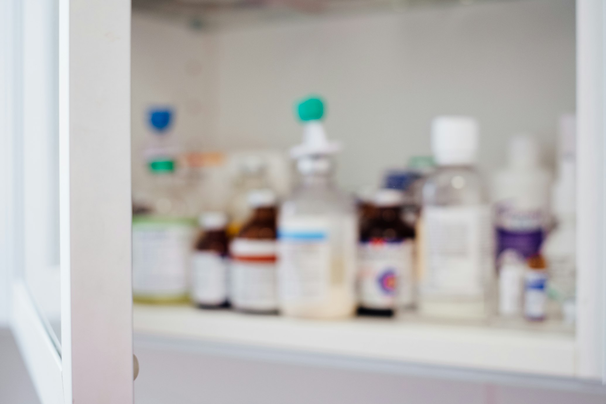 A pharmacist in a white lab coat organizing various medication boxes on well-stocked pharmacy shelves.