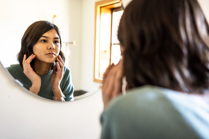 A woman closely examining her clear and healthy skin in a mirror.