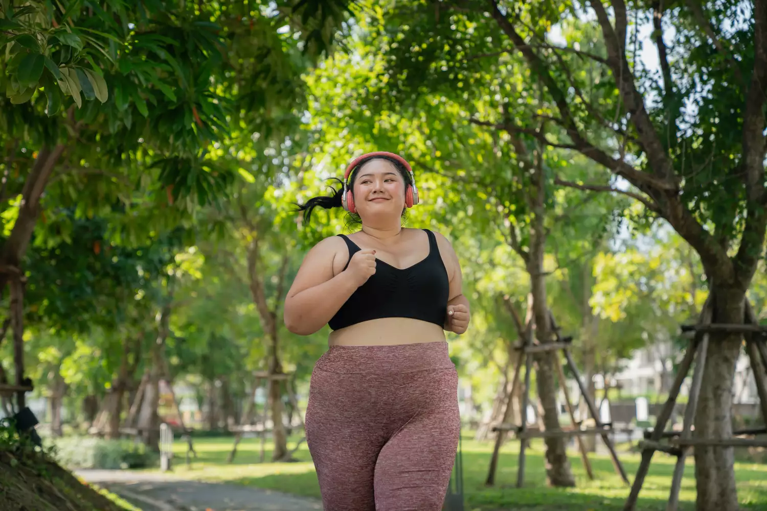 A smiling woman jogging in a park, representing a healthy and active lifestyle.