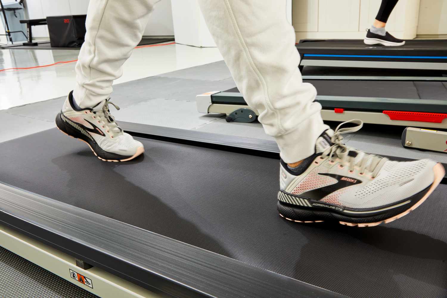 A runner performing a gait analysis on a treadmill in a clinical lab setting while wearing Brooks running shoes.