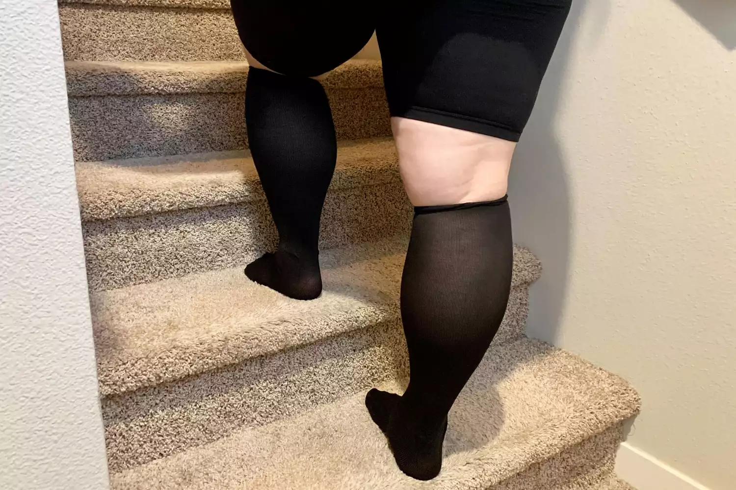 Person wearing black knee-high compression socks walking up a set of stairs.