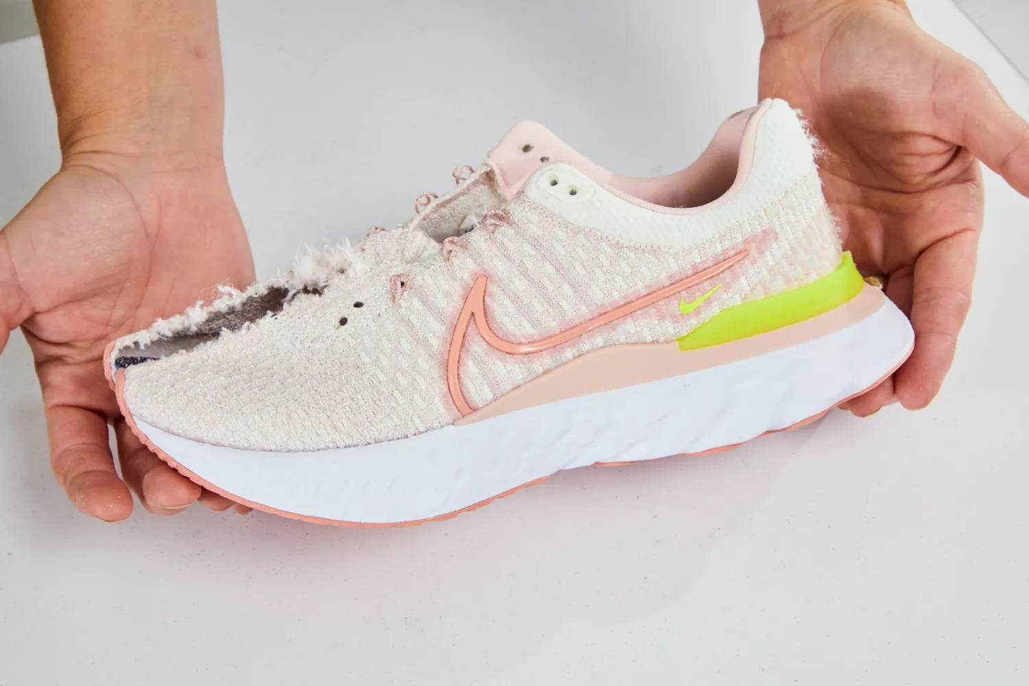Hands holding a worn-out running shoe showing significant wear on the fabric and compression in the midsole.