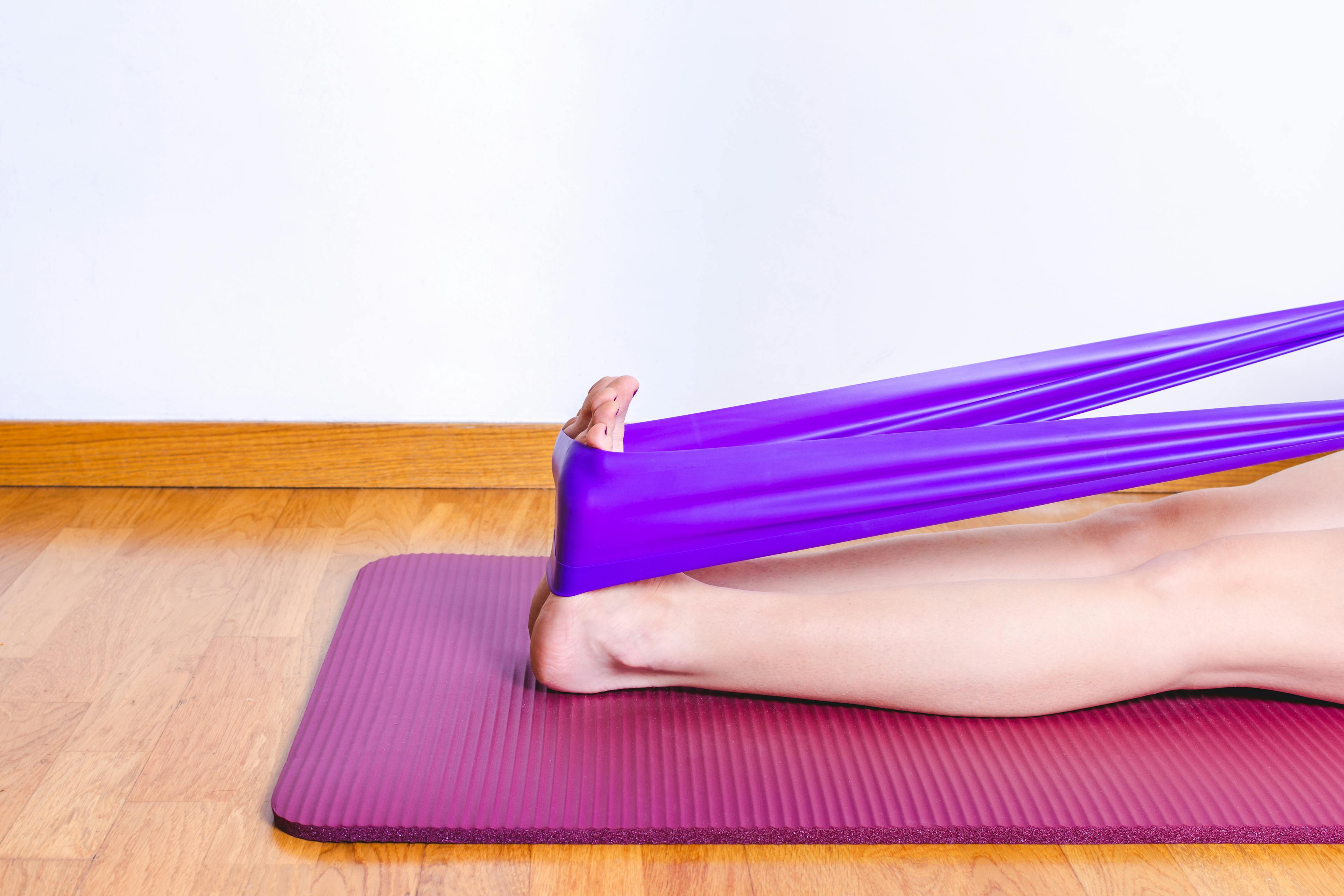 A person seated on the floor using a towel wrapped around the foot to perform a calf and arch stretch.