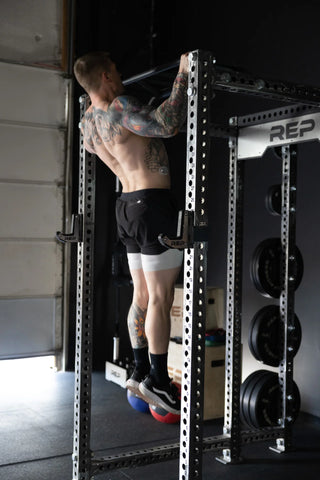 A man performing pullups on a bar as a bodyweight alternative to lat pulldowns.