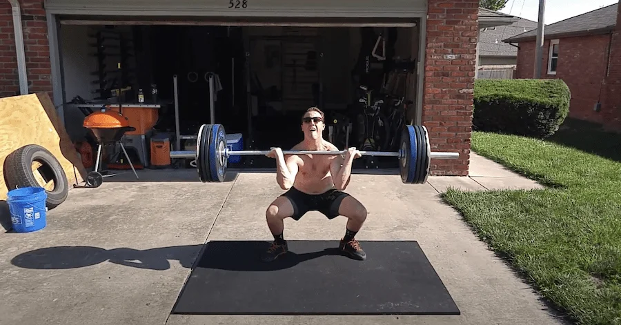 A man performing a barbell clean on a heavy-duty rubber horse stall mat.