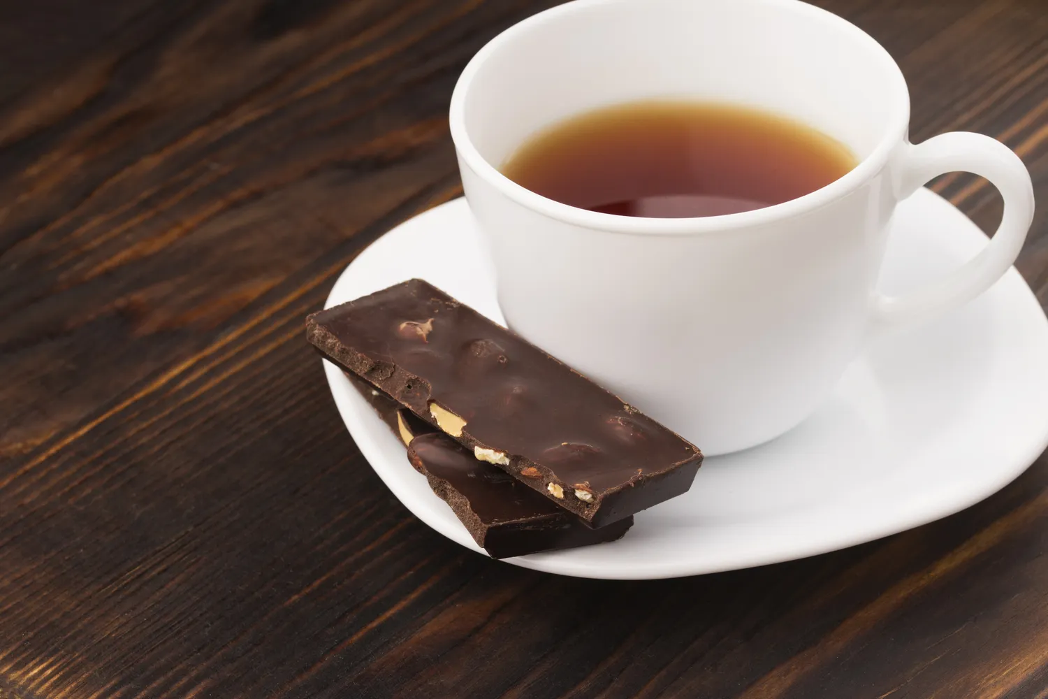 A cup of herbal tea served with a small piece of dark chocolate.
