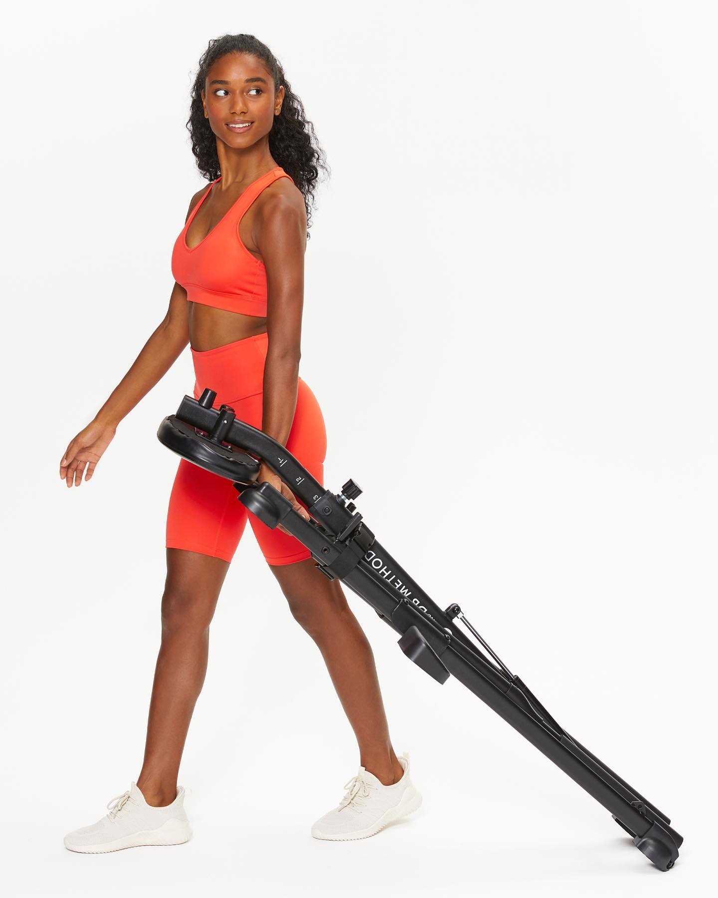 A woman easily carrying a compact home squat machine outdoors.