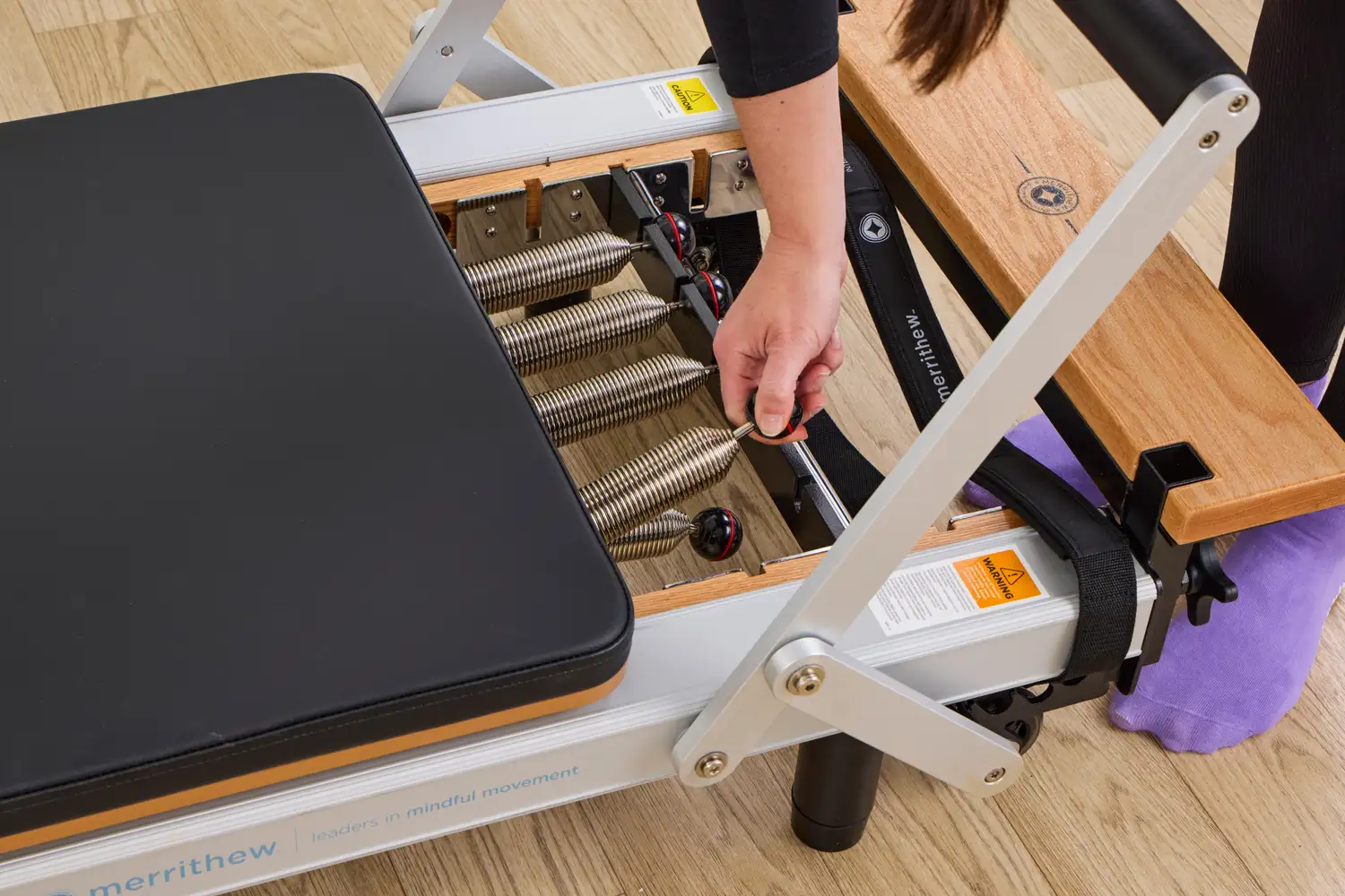 A close-up shot of a person's hand adjusting the tension springs on a Merrithew SPX Reformer.