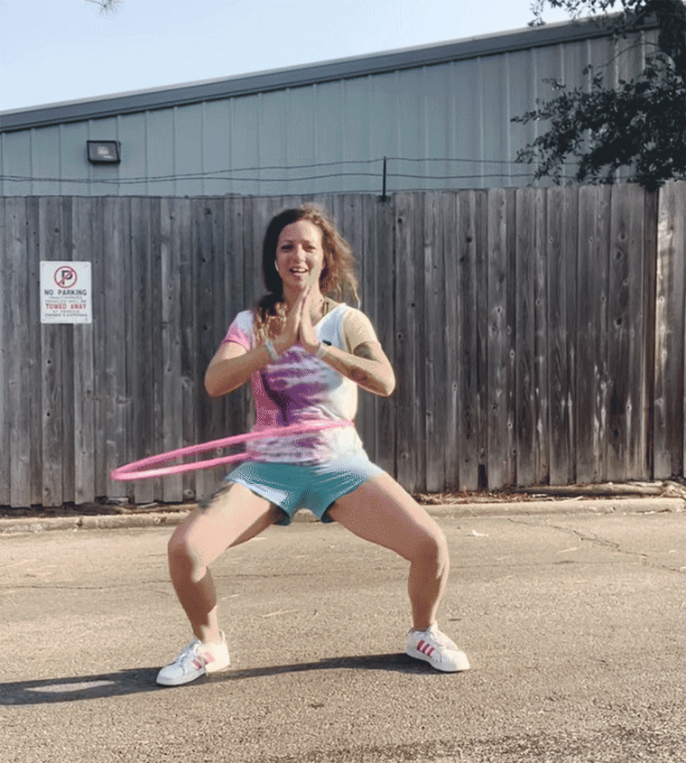 A woman performing a squat while keeping a weighted hula hoop spinning around her waist.