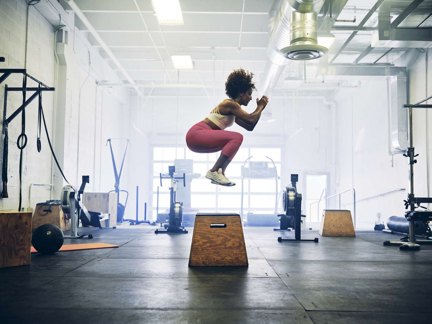 A female athlete performing a high-velocity box jump in a gym setting.