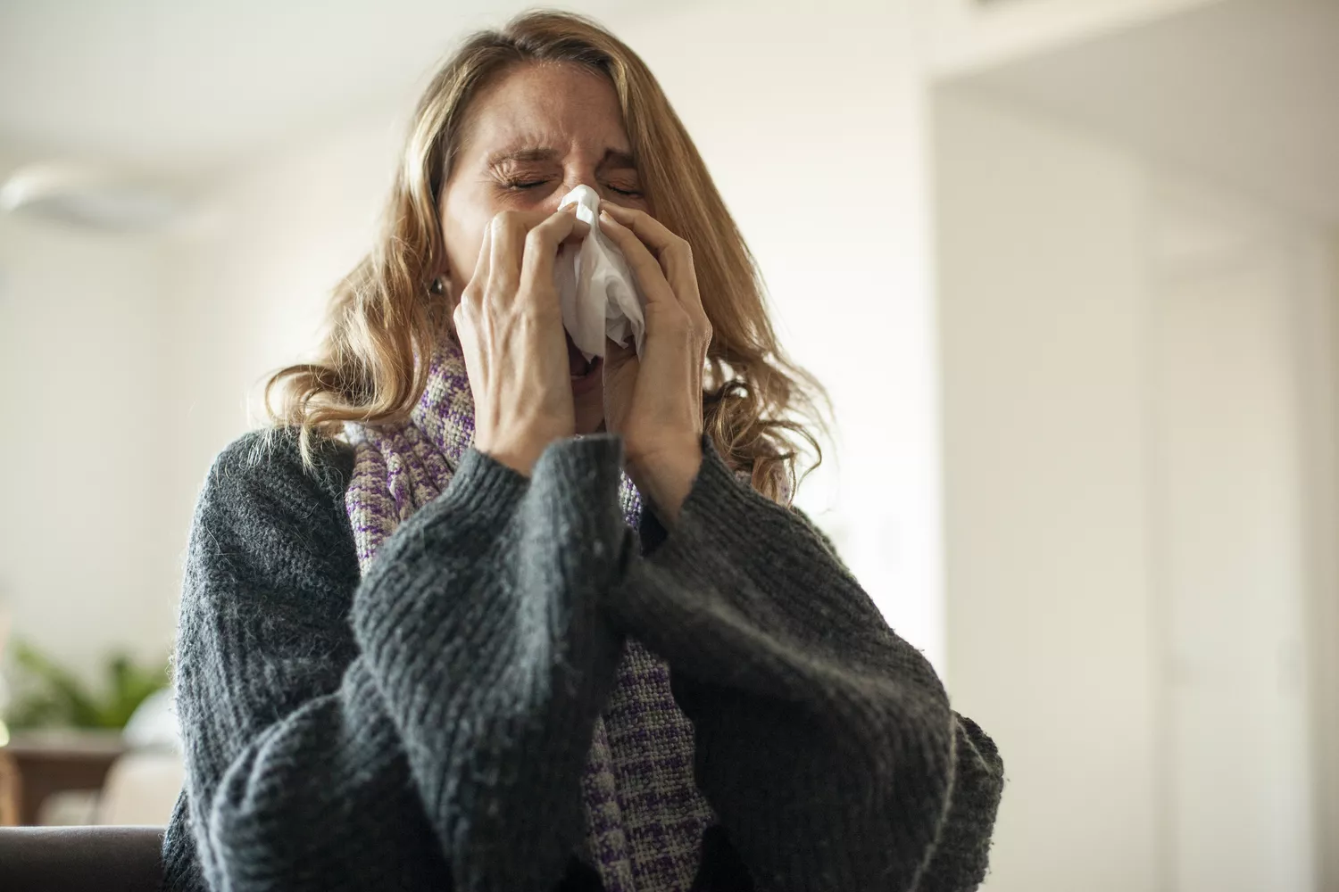A middle-aged woman looking fatigued and blowing her nose, representing the physical toll of lifestyle stress.