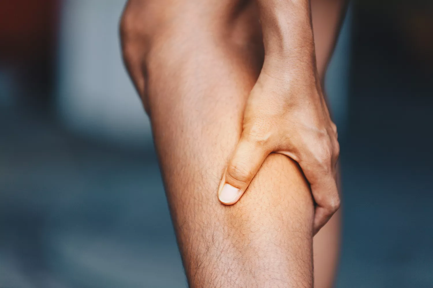 A person sitting down and clutching their painful calf muscle in distress.
