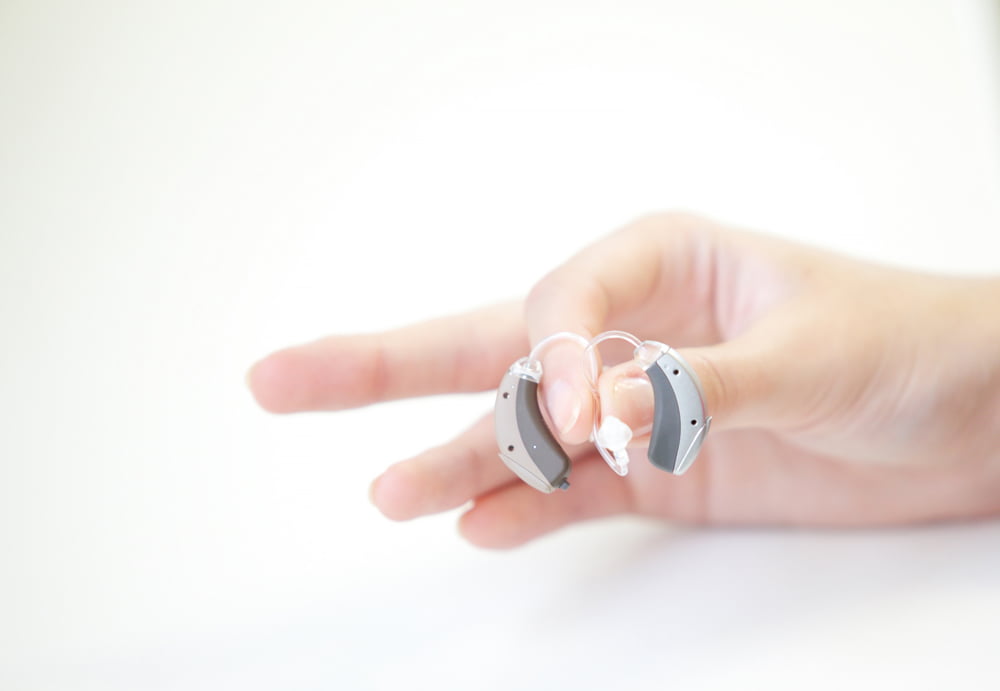 A close-up of a hand holding several traditional air-conduction hearing aids.