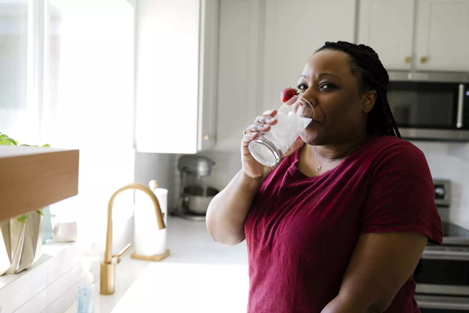 A woman in a bright kitchen drinking a glass of water, representing the lifestyle habits that support better digestion and sleep.