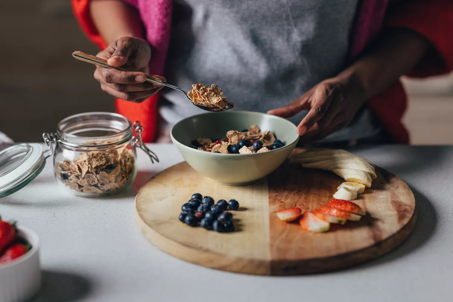A person preparing a healthy breakfast bowl with fresh fruit and whole grains.