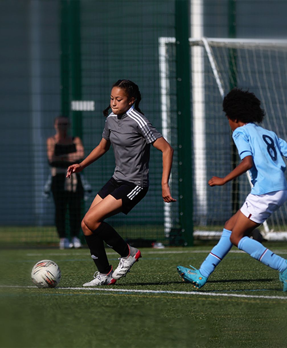 A female player dribbling the ball while being closely guarded by an opponent during training.