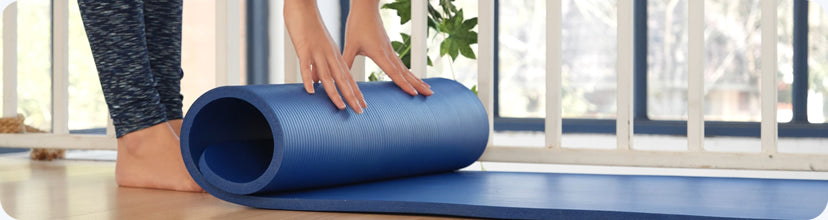 A person using a foam roller on a yoga mat in a home setting.
