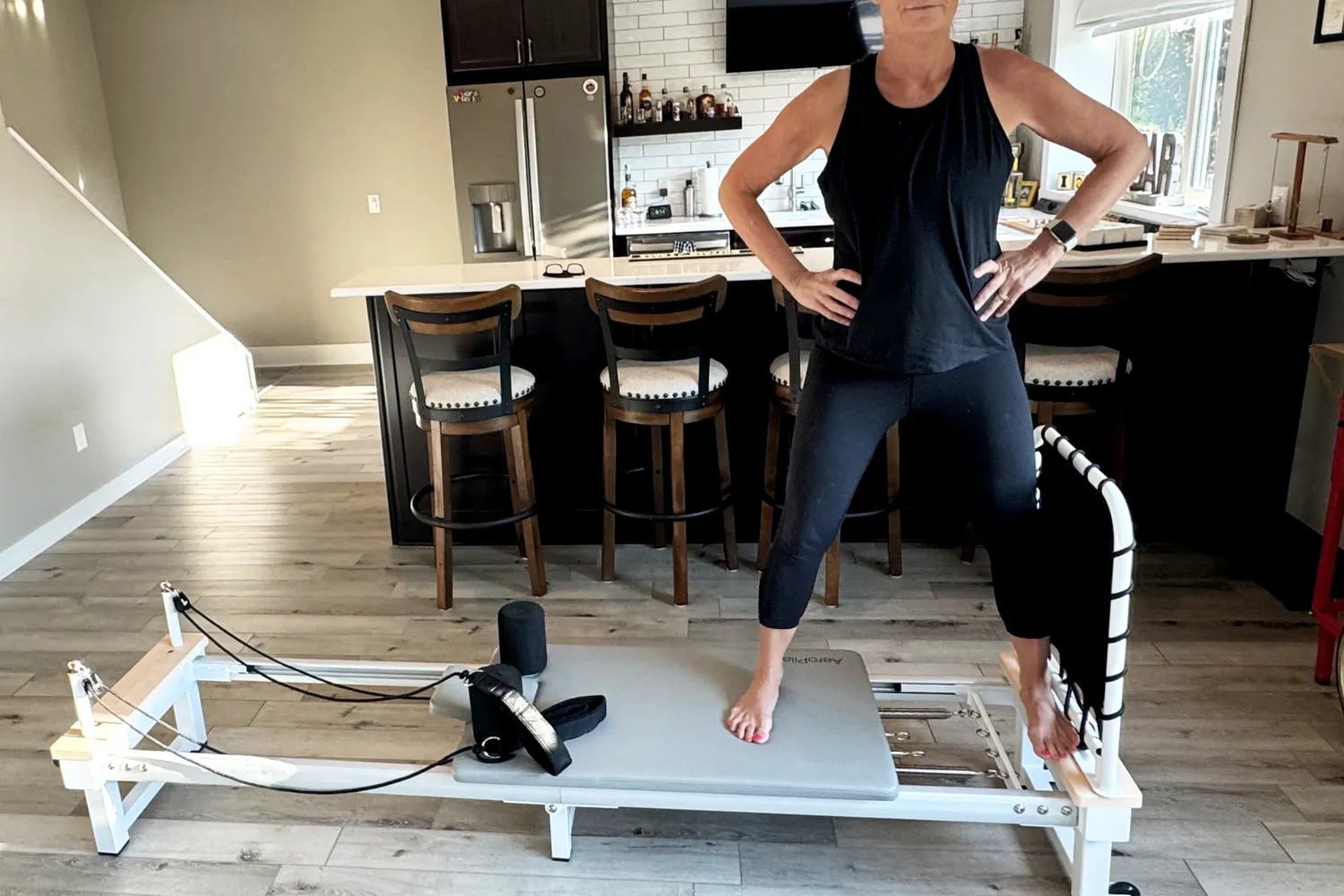 A person performing a leg exercise on an AeroPilates Precision Series reformer on a wooden floor.