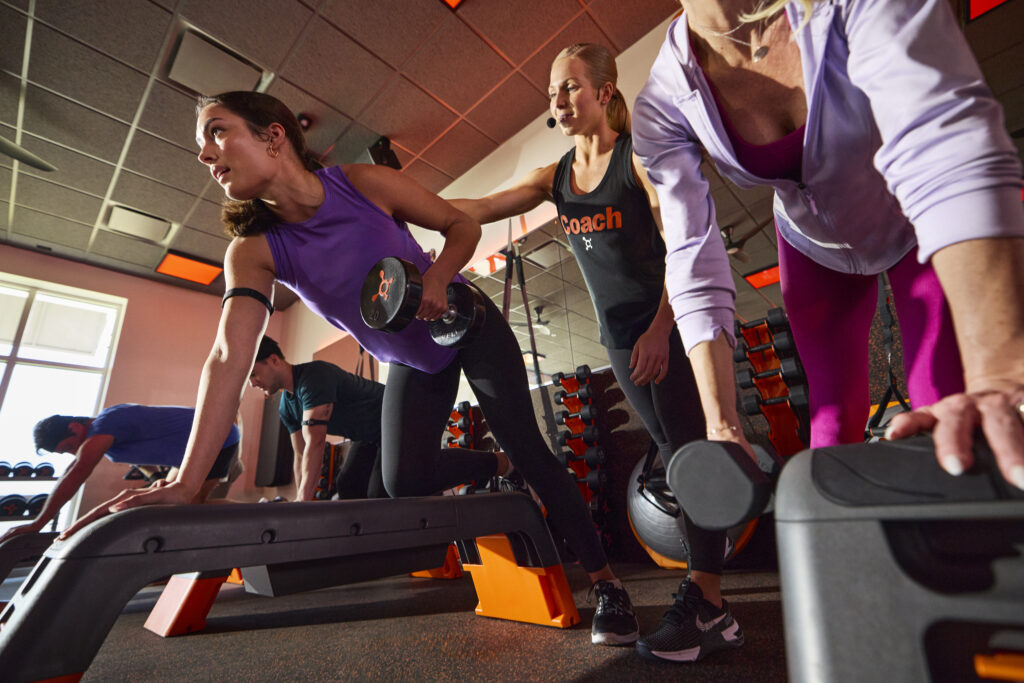 A wide shot of a group of people exercising in an Orangetheory Fitness studio during a high-intensity session.