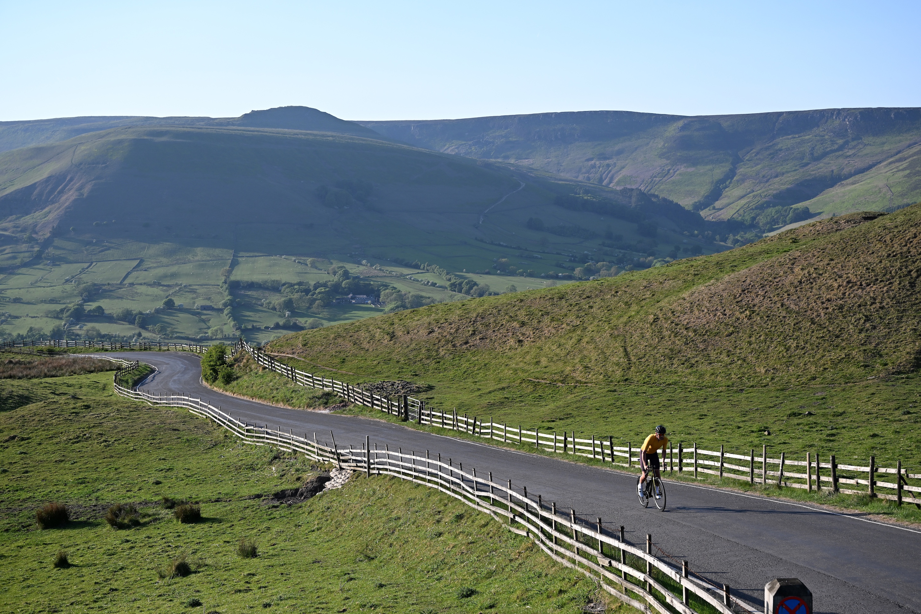 A road cyclist in a white jersey climbing the winding Mam Tor road in the Peak District.