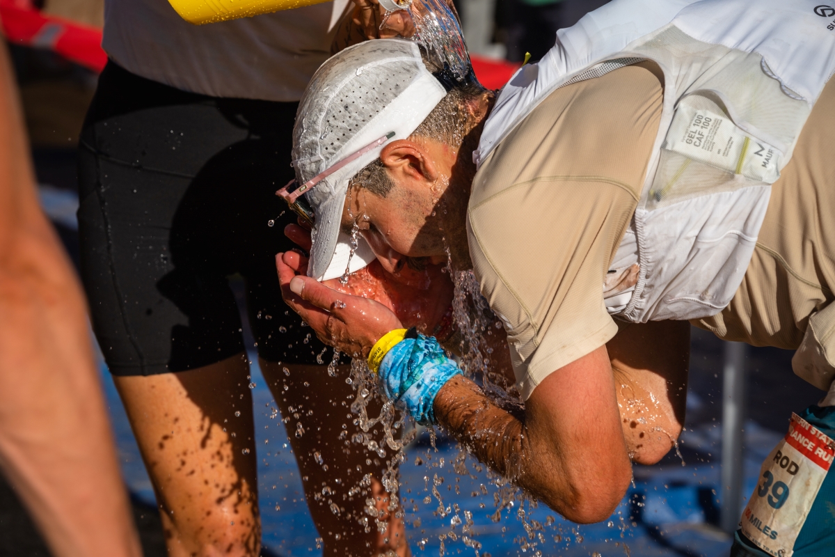 An ultrarunner dousing himself with water at a race aid station.