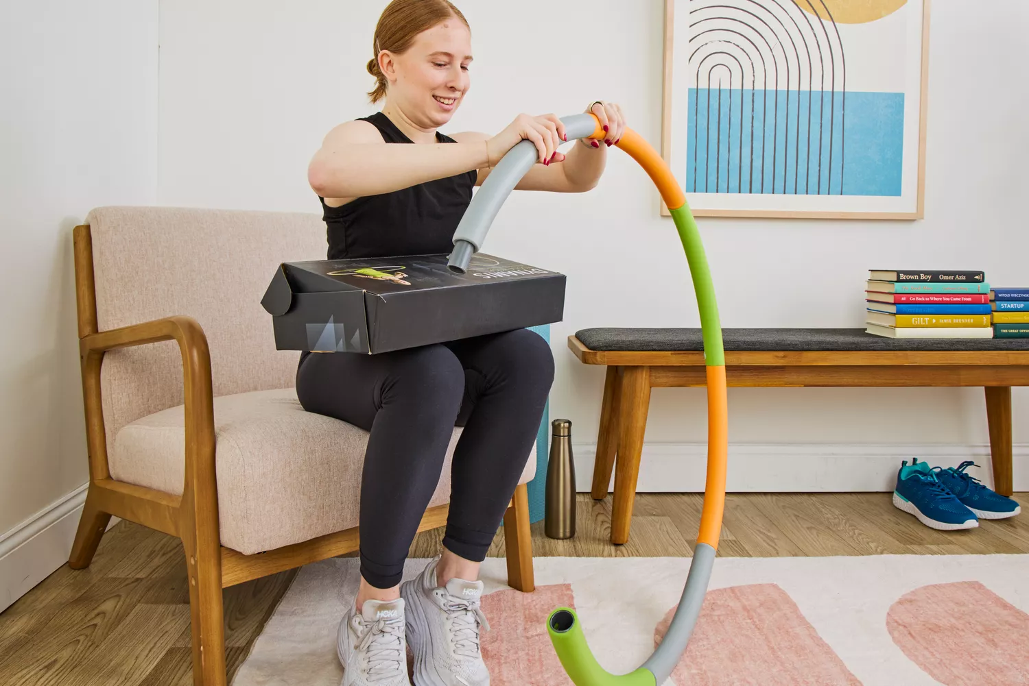 A woman sitting on a chair and smiling while assembling colorful hula hoop segments from a product box.