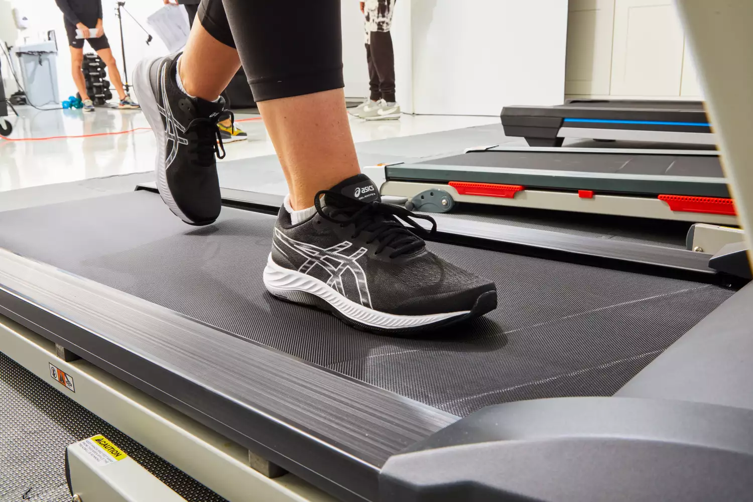 A person undergoing a professional gait analysis while walking on a treadmill in a lab environment.