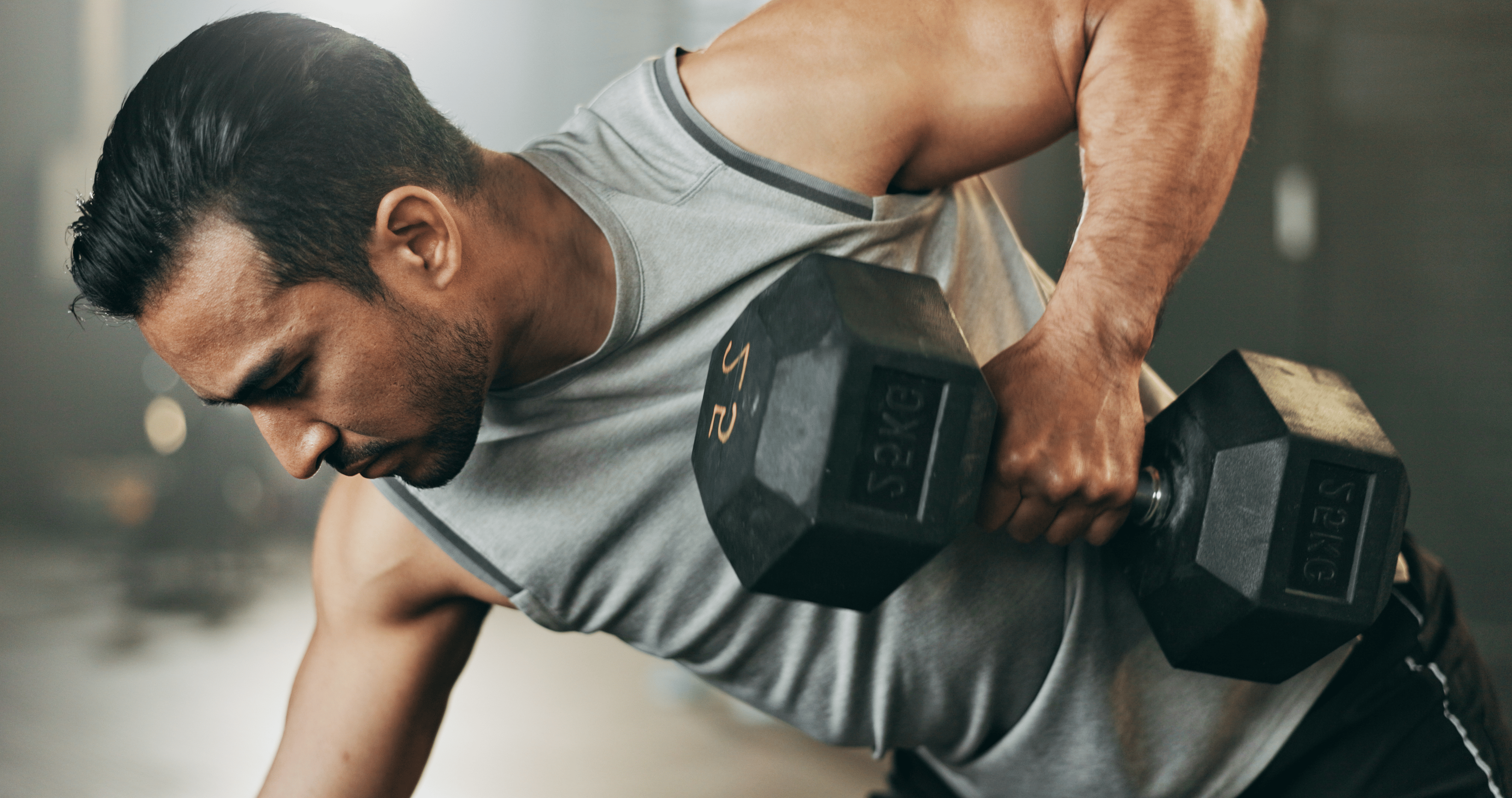 A man performing a heavy dumbbell press in a gym environment.
