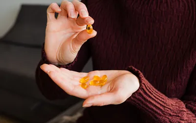 A person in a maroon sweater holding yellow softgel vitamin supplements.