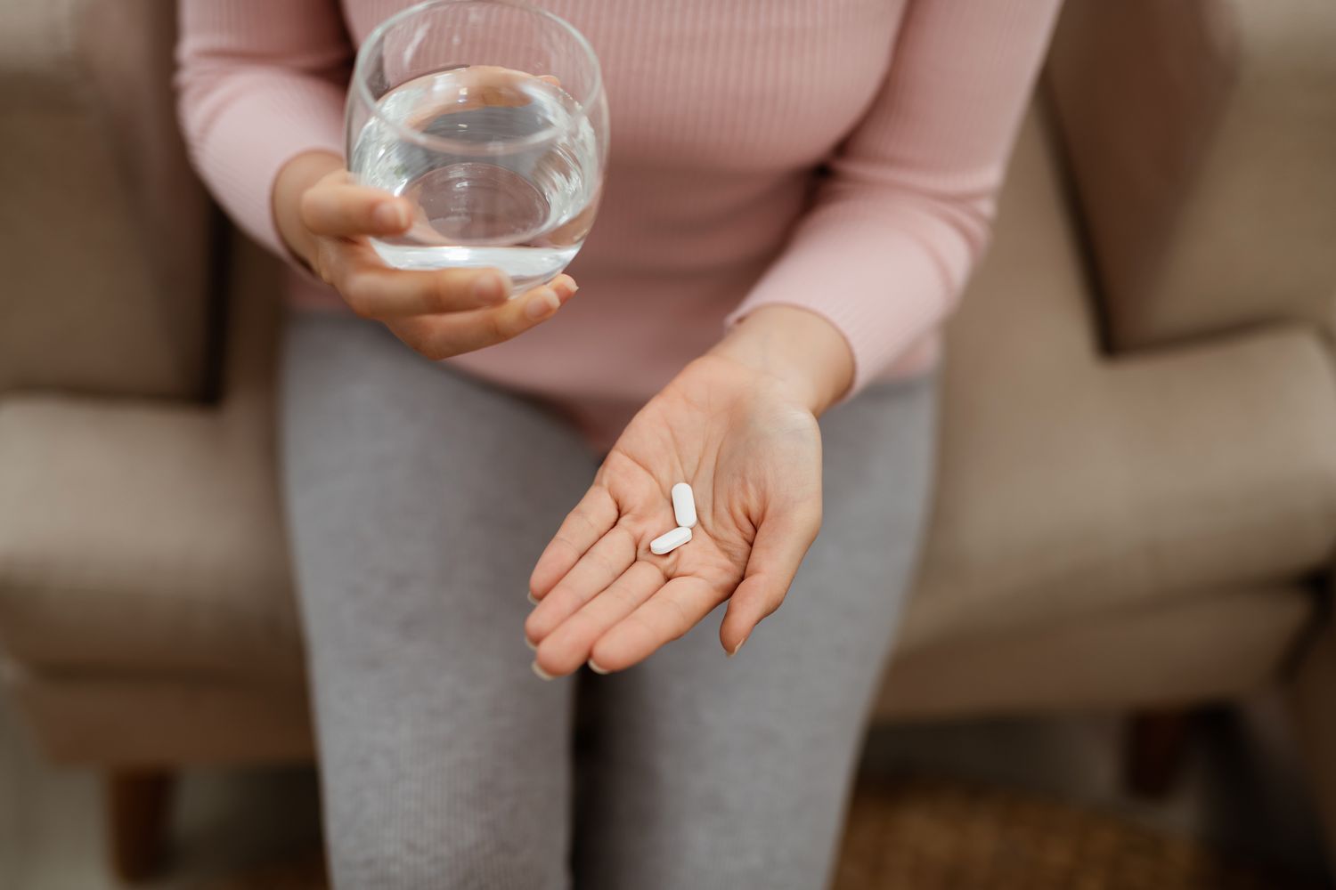 A person holding a vitamin capsule in their palm next to a glass of water.