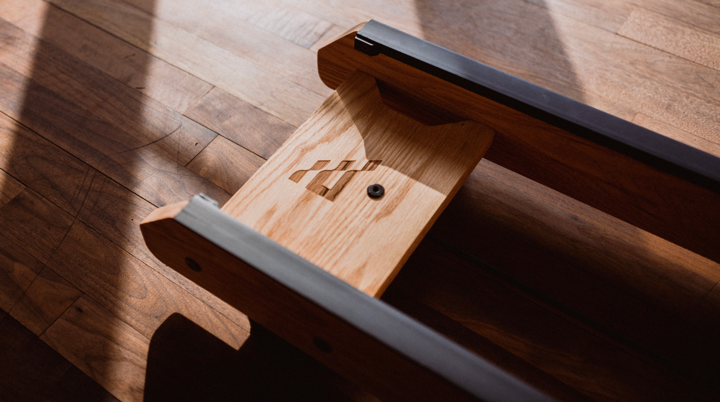 Close-up of polished hardwood rowing machine rails showing detailed wood grain and construction.