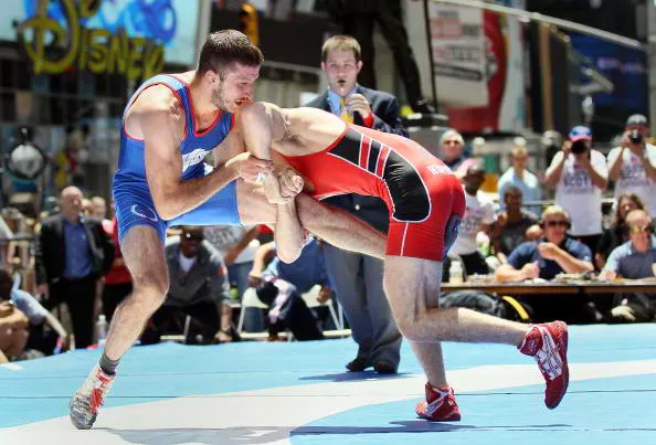 Olympic wrestlers in a high-intensity match on a competition mat.